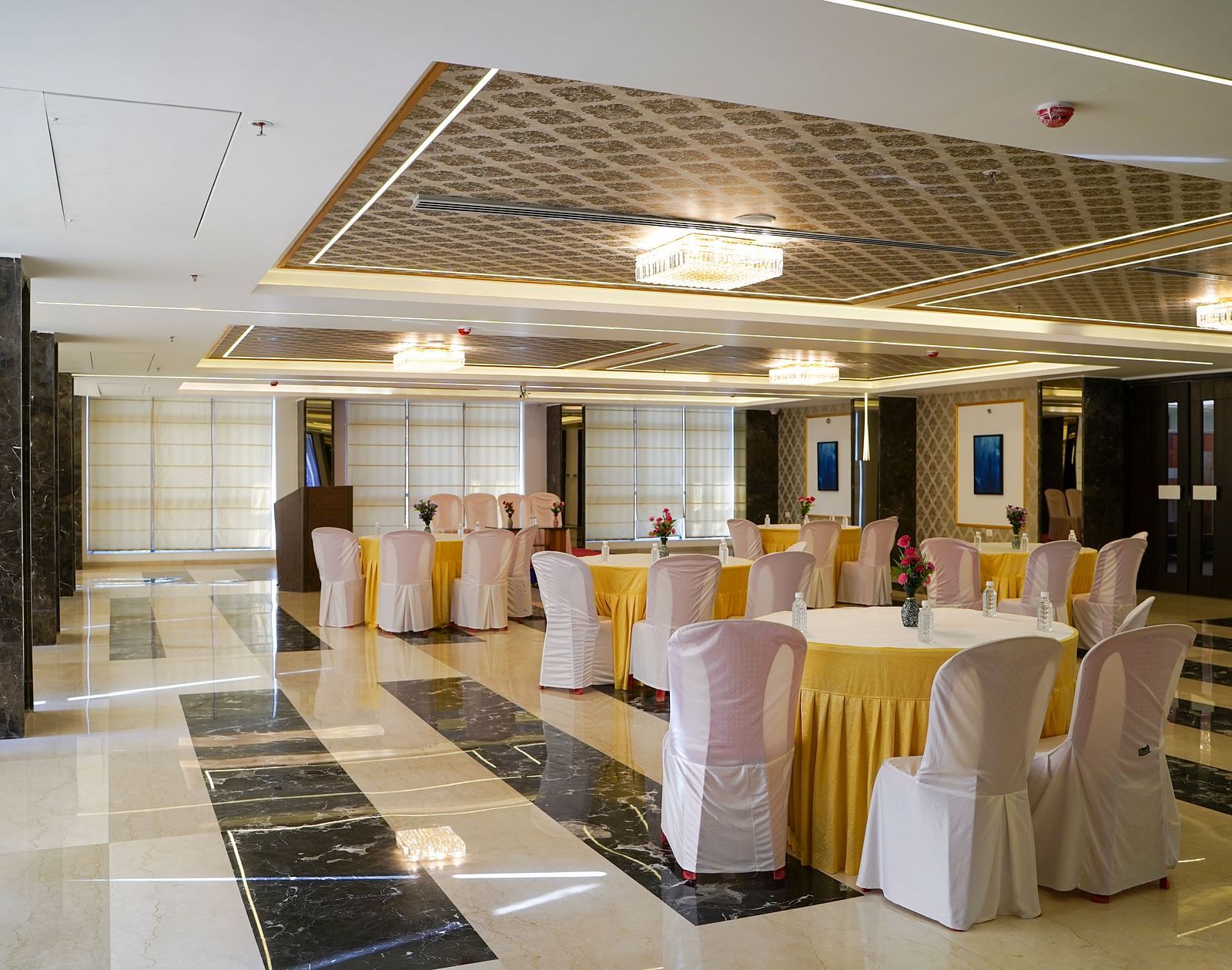  A decorated banquet hall at BNGV Grandeur Hotel and Banquets, with round tables draped in white and gold, and chairs for a reception.