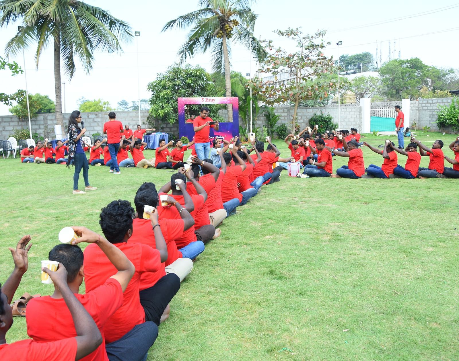 Group of people with red t-shirts seated in a line on a grass in an outdoor lawn with green trees at Grande Bay Resort & Spa.