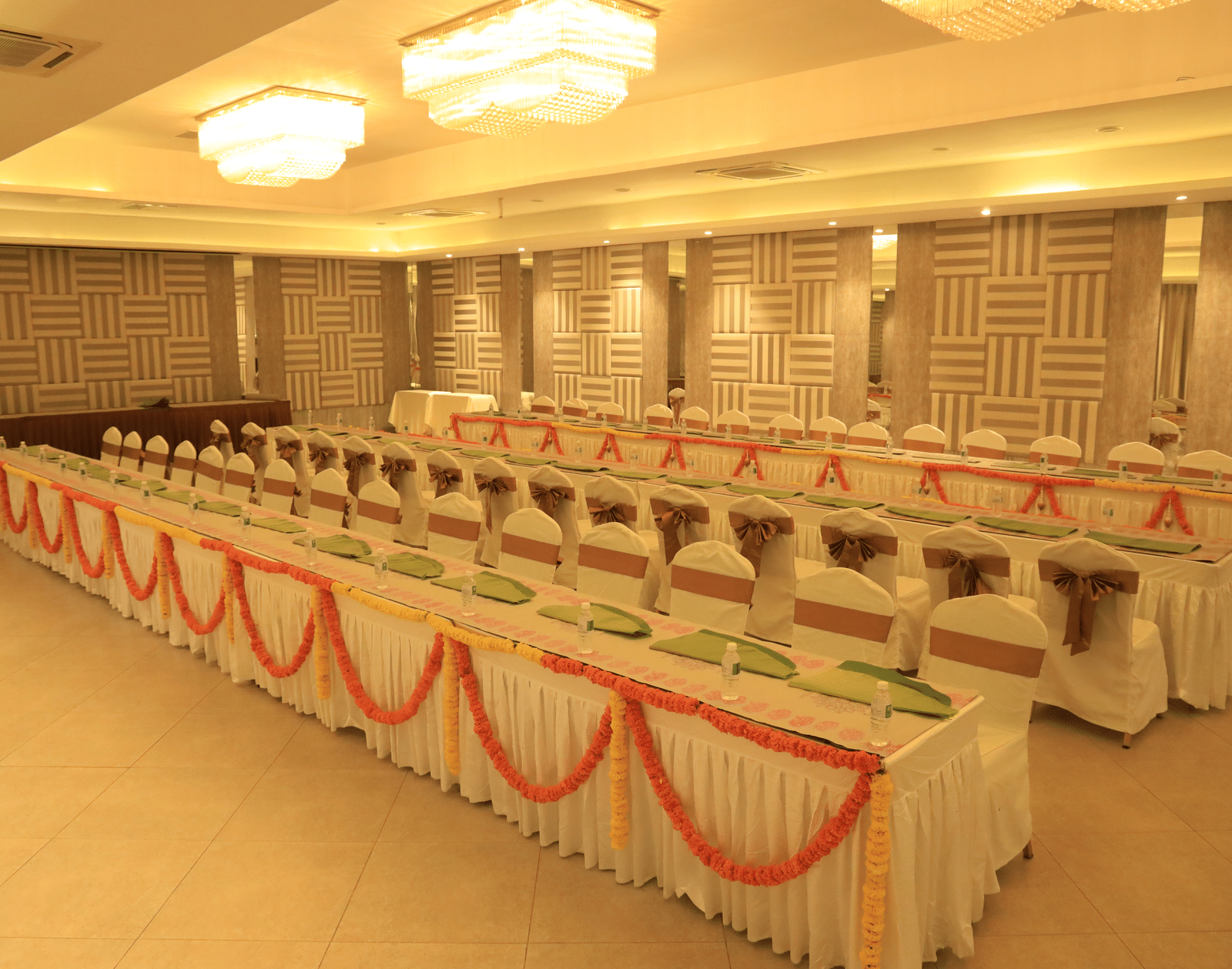 A spacious indoor hall set up with long tables and chairs, adorned with sashes and colourful table runners, ready for a large event or conference - Grande Bay Resort & Spa, Mamallapuram