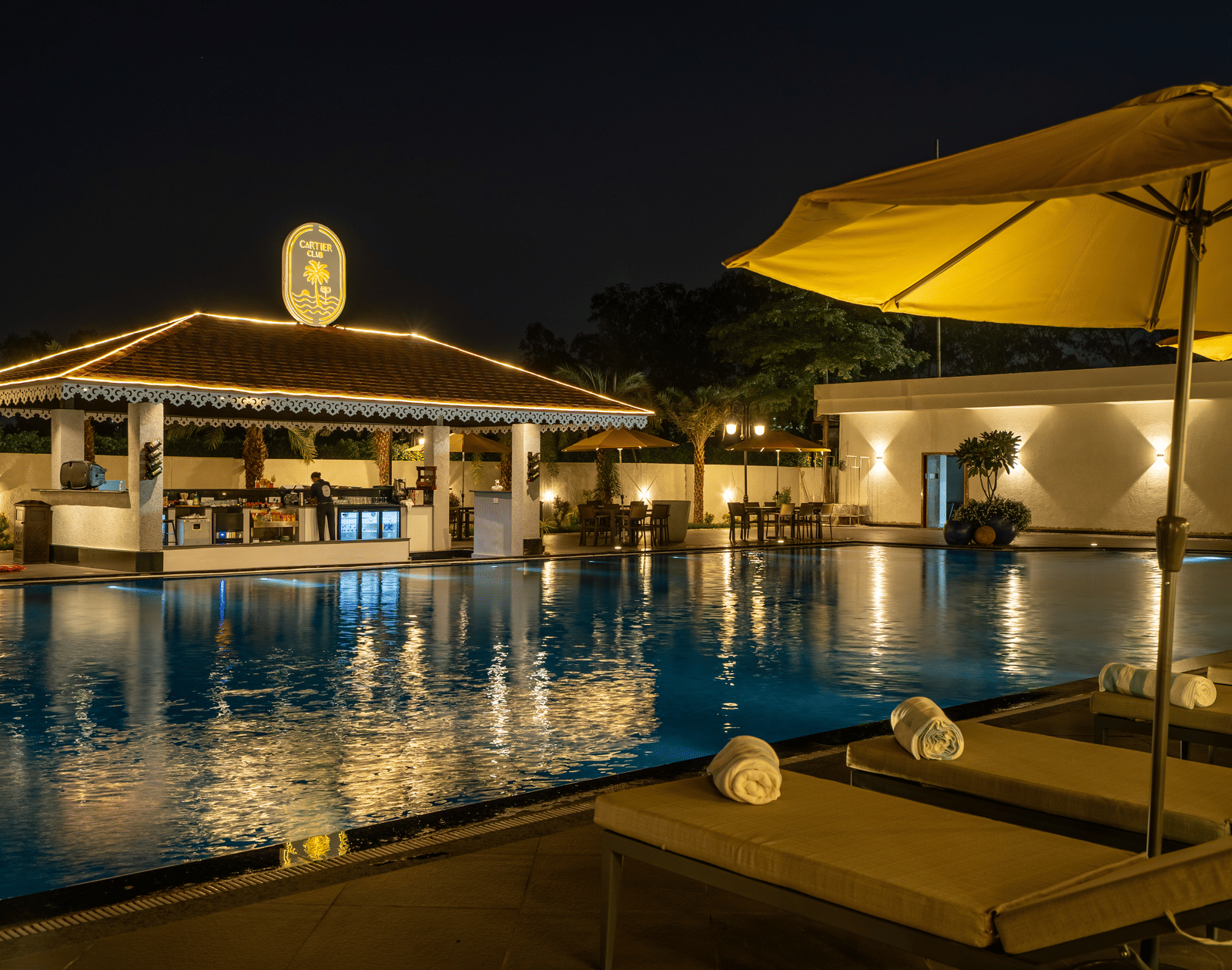 Evening view of the swim-up bar area next to the pool, featuring seating and ambient lighting under an umbrella at Hotel Hukam's Lalit Mahal.