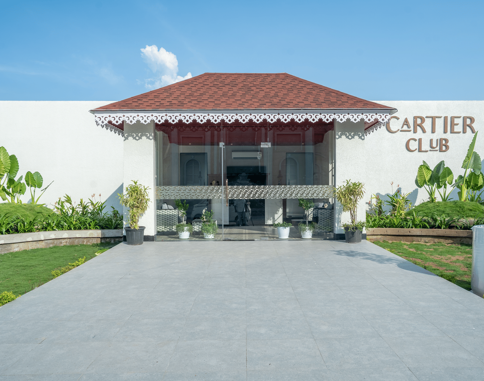 Exterior of the 'Cartier Club' building, a white structure with a red roof, fronted by a paved walkway and green lawn at Hotel Hukam's Lalit Mahal.