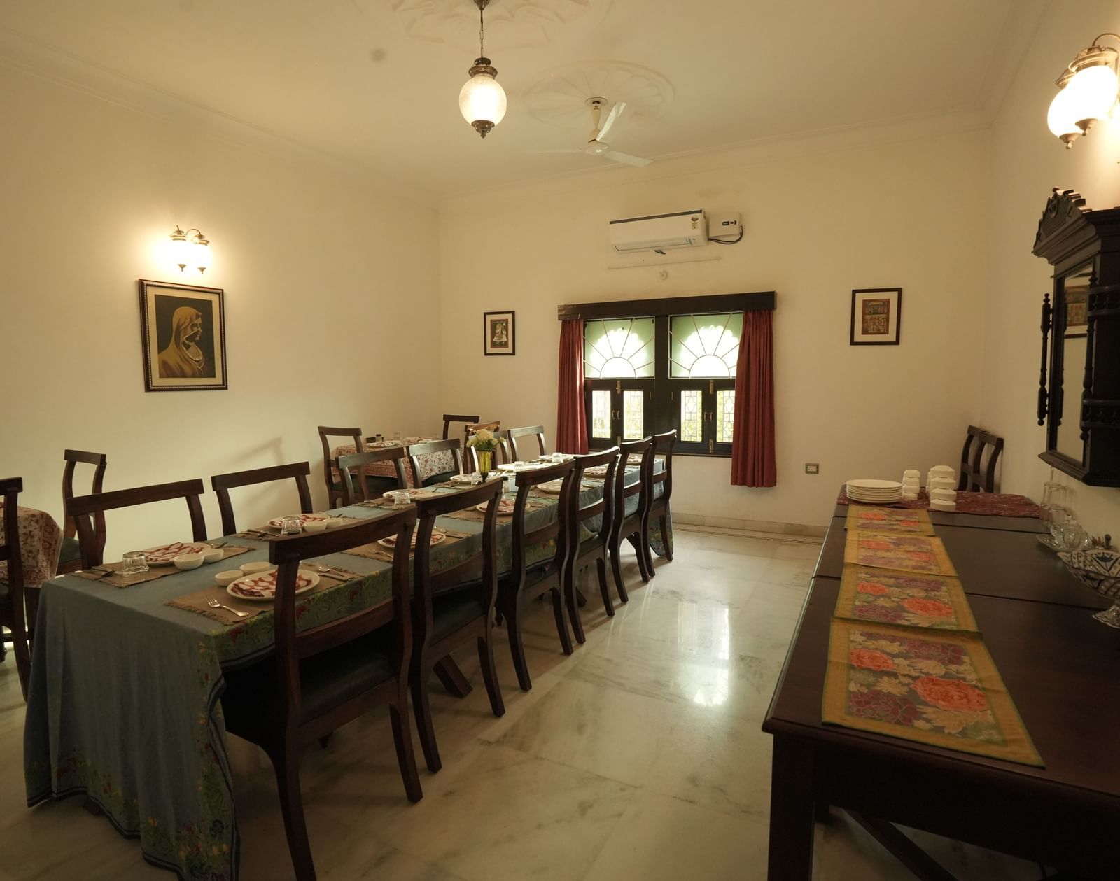 A wide, eye-level shot of a large dining room at Mahendra Niwas with a long table set with chairs. The room has light walls and marble floors.