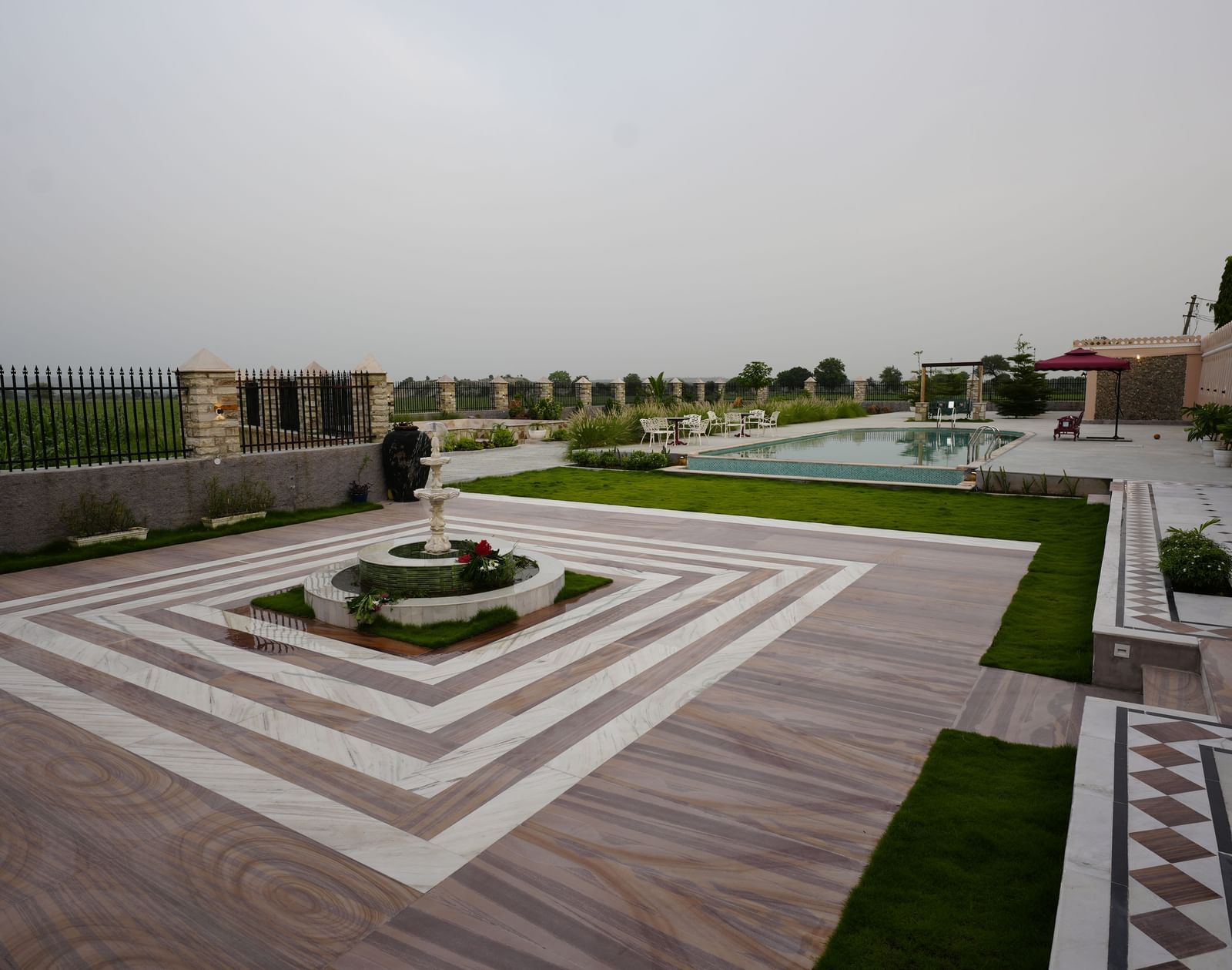 An eye-level shot of a building with a large courtyard and manicured gardens. A walkway with a diamond pattern in the center leads to a small garden at Mahendra Niwas.
