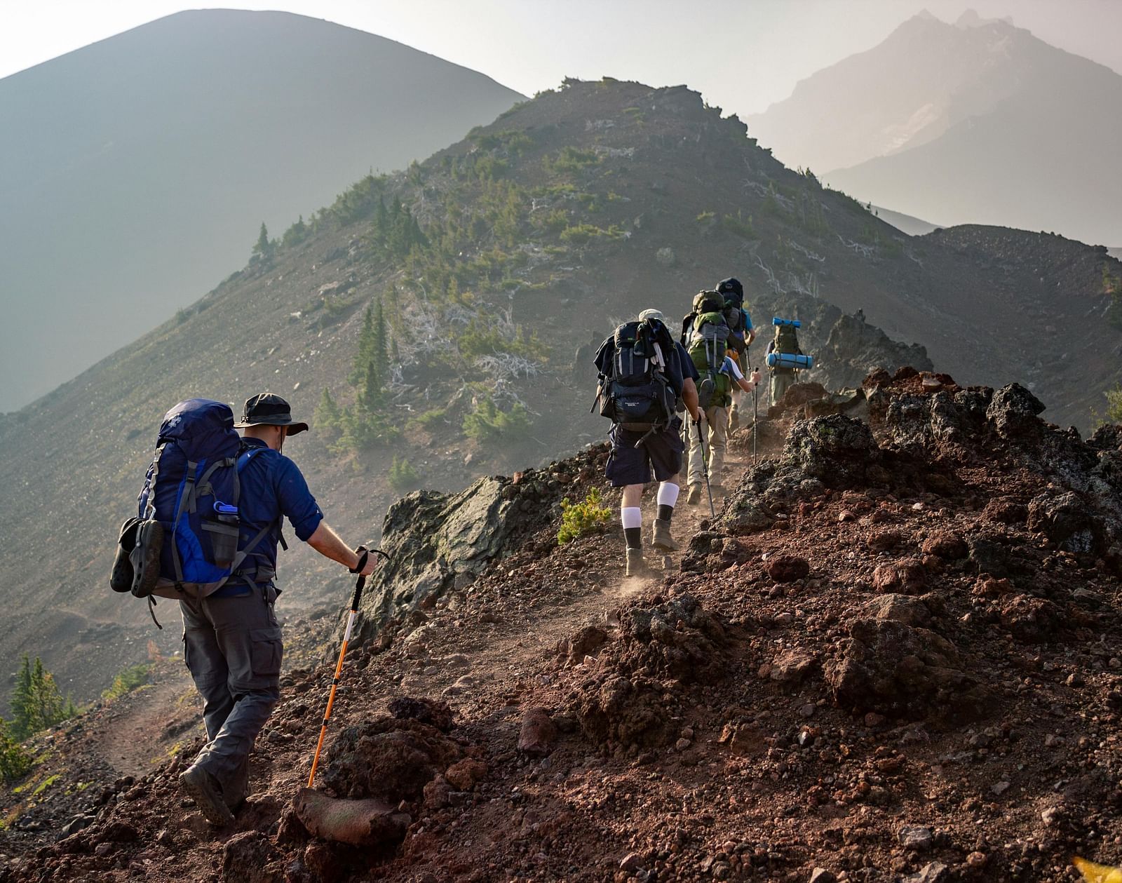A group of hikers trekking along a rocky mountain trail with backpacks and trekking poles.
