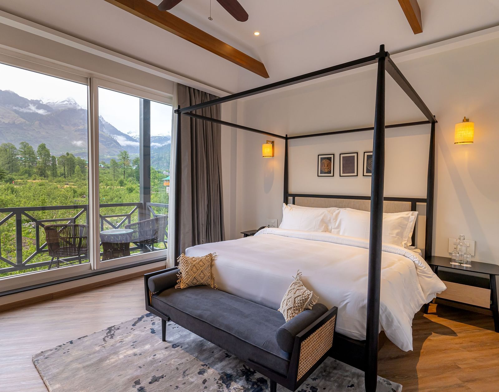 Spacious wooden-framed bed with seating at the foot and a large glass door opening to mountain views at Nivasana Manali.