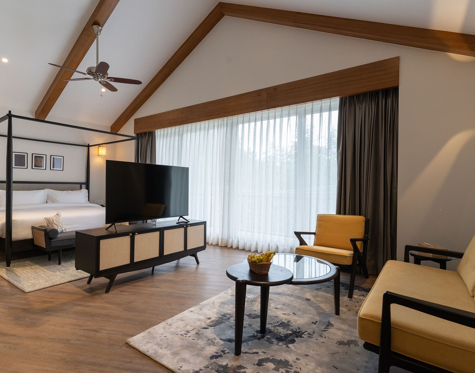 Spacious room with wooden-framed bed, cushioned sofa, and a TV placed on a wooden table at Nivasana Manali.
