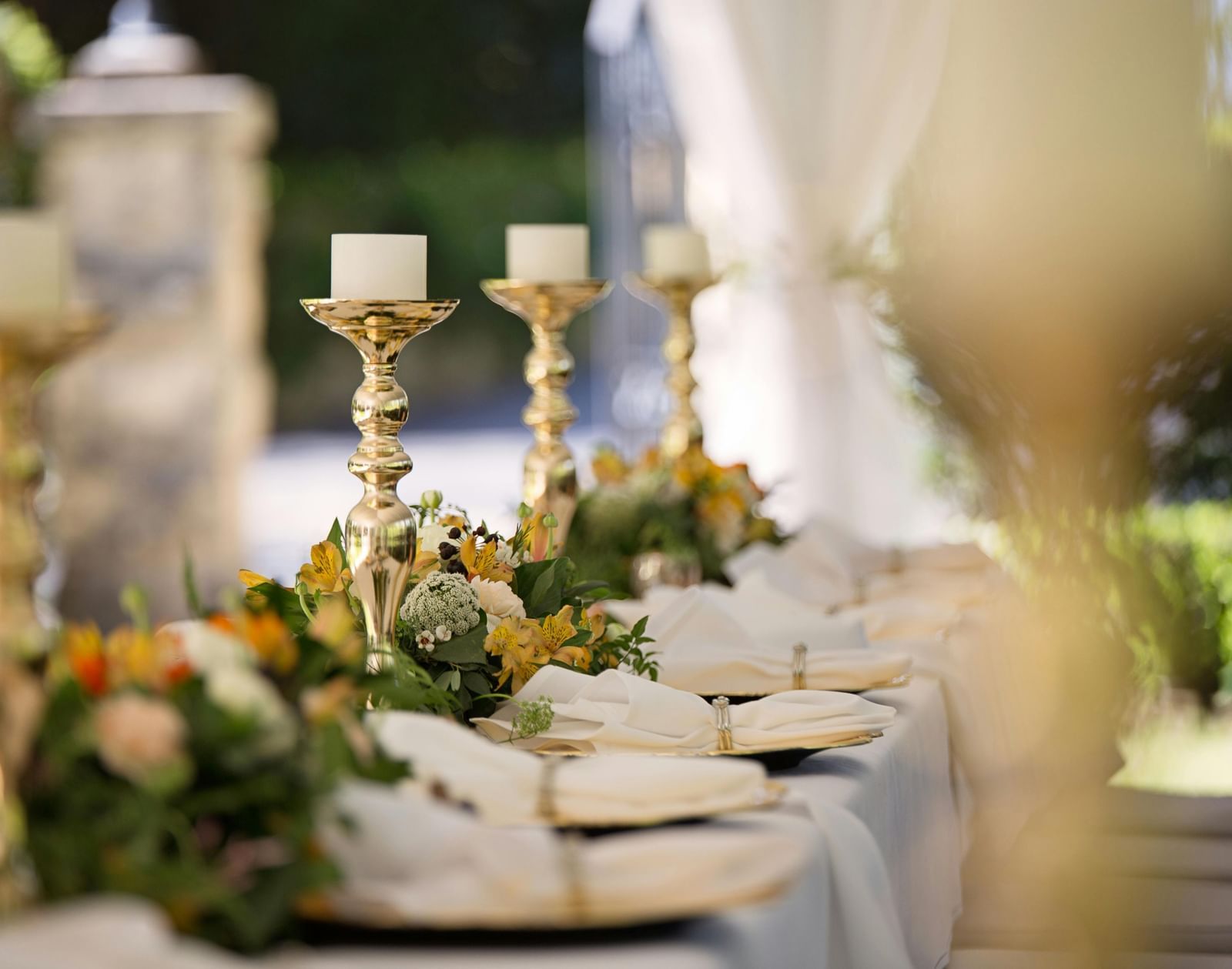 A long table covered with a table cloth decorated with shinny candle stands and well-arranged cutlery.