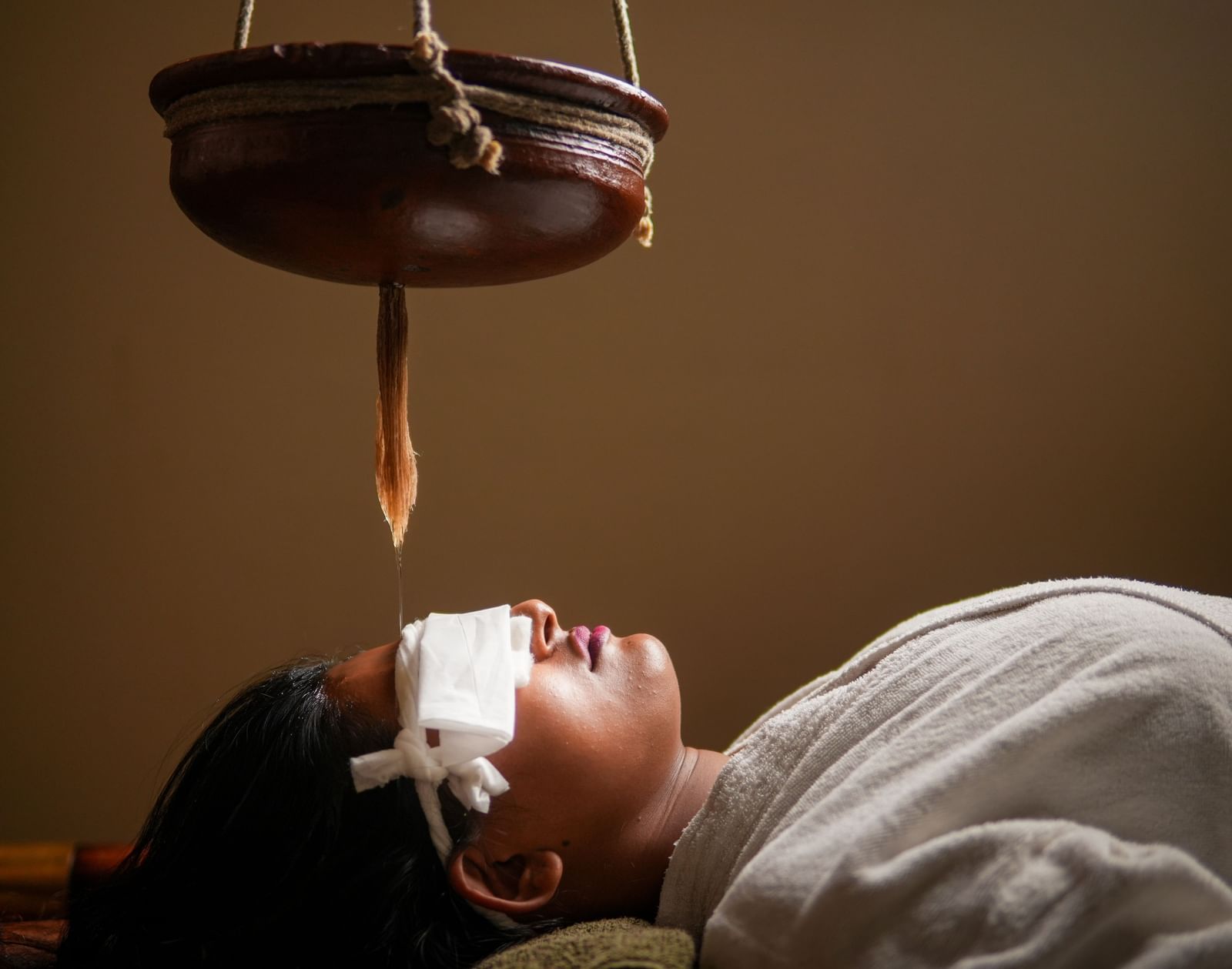 Shirodhara therapy in Vedic Village Spa Resort, featuring a stream of oil on a client's forehead.