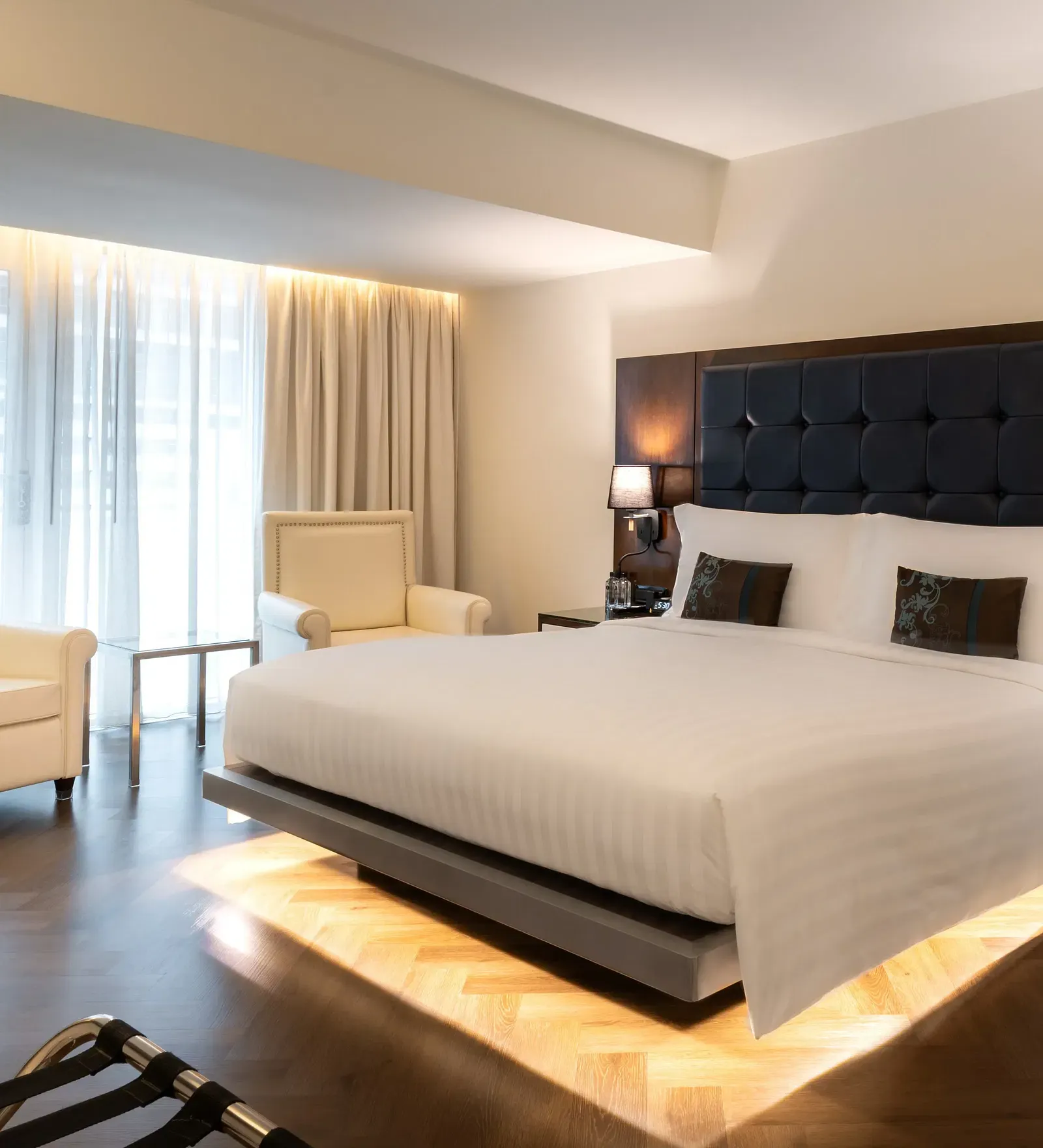 Luxury suite with platform bed, under-bed lighting, and lounge chair at Night Hotel Bangkok.