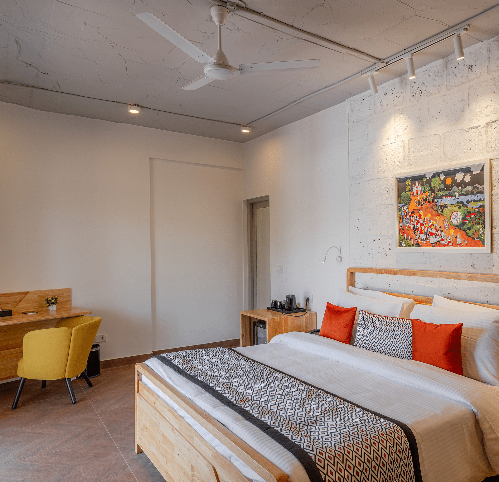 An image of hotel room with king size bed, painting on the wall, work desk and chair at one corner and a bedside table  at Bedzzz Xclusiv Morjim, Goa