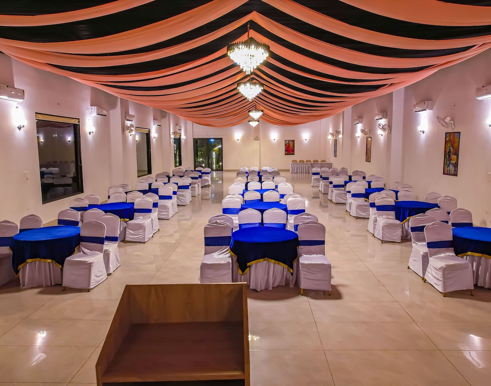A long indoor dining hall at Vedikant Resorts The Mallard Corbett shows rows of tables and chairs beneath a decorated ceiling.