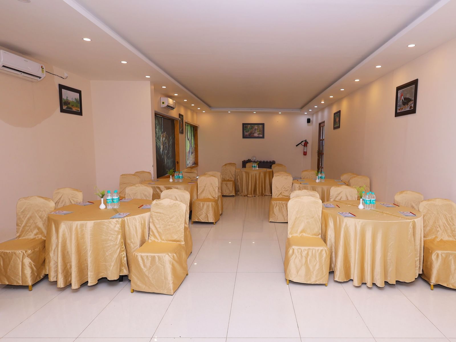 An empty banquet hall set up with tables and chairs draped in white and yellow linen at Corbett Nirvana Resort.