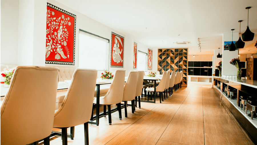 Daylit dining hall with long tables, cream chairs, red folk-art panels and a buffet counter at Tandoori Tamashaa, Ilara Hotels & Spa, Tada.