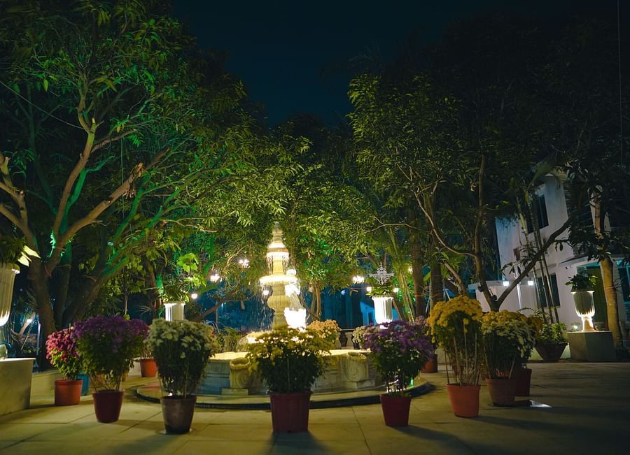 A image of a huge lawn with trees and there is also a fountain surrounded by flower pots at Tangamati Garden Resort