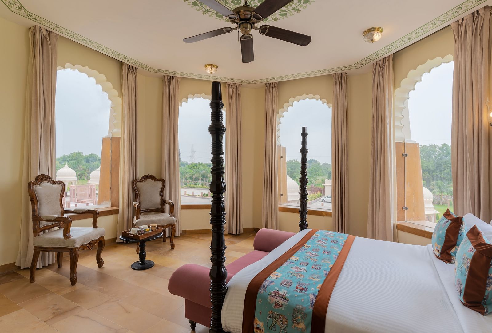 Elegant bedroom with arched windows overlooking scenic landscape at Kesar Bagh Palace.