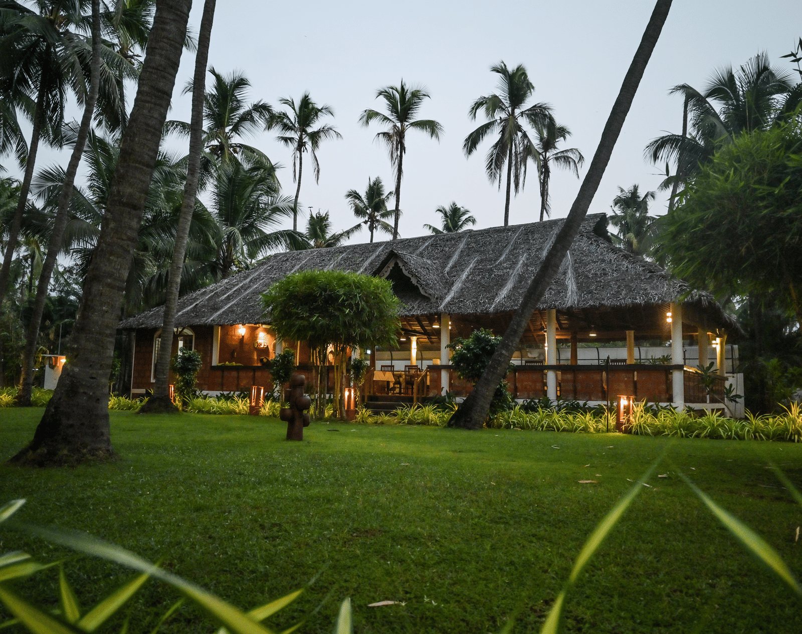 The lush green grounds of Ayur On The Beach Nattika with a traditional villa in the background.
