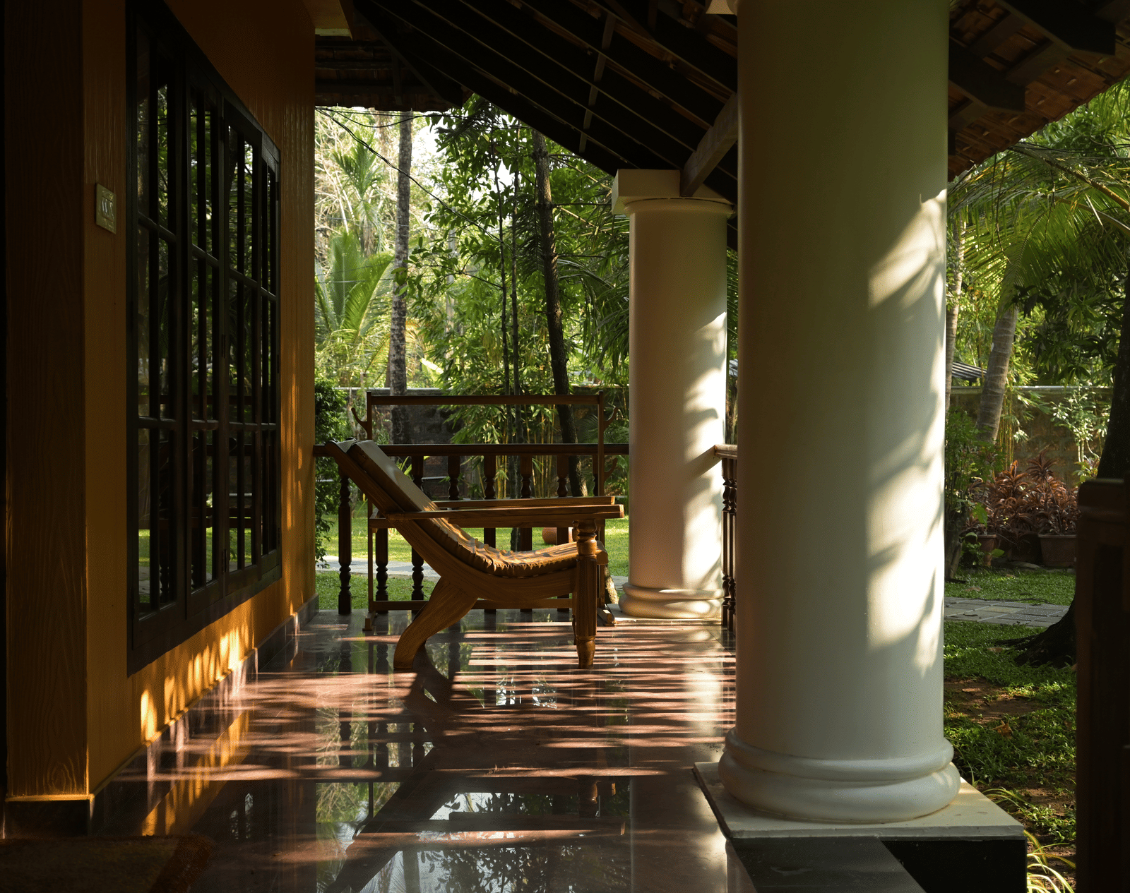 A tranquil villa verandah at Ayur On The Beach Nattika featuring large white pillars and traditional wooden furniture.