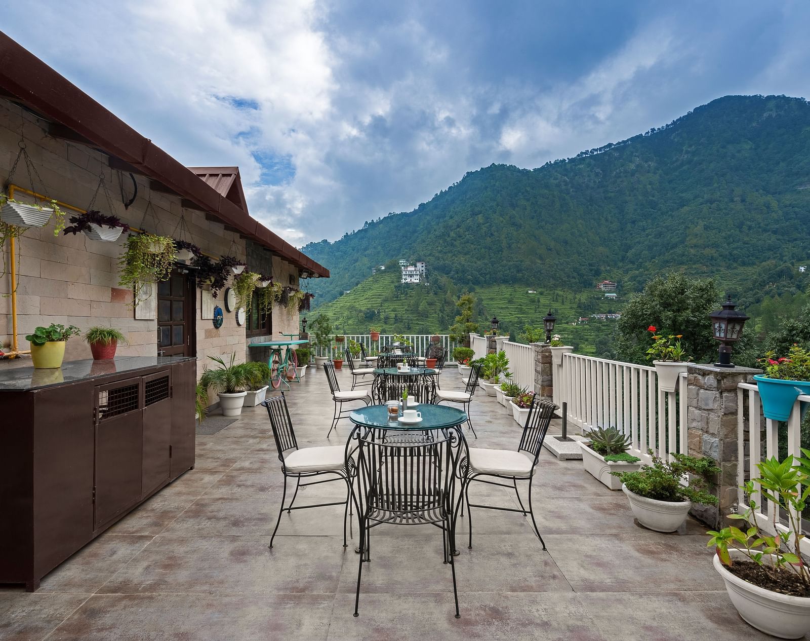 Rooftop dining area with mountain views under a cloudy blue sky, at BluSalzz Collection - Suvaasa Resort, Ramgarh.
