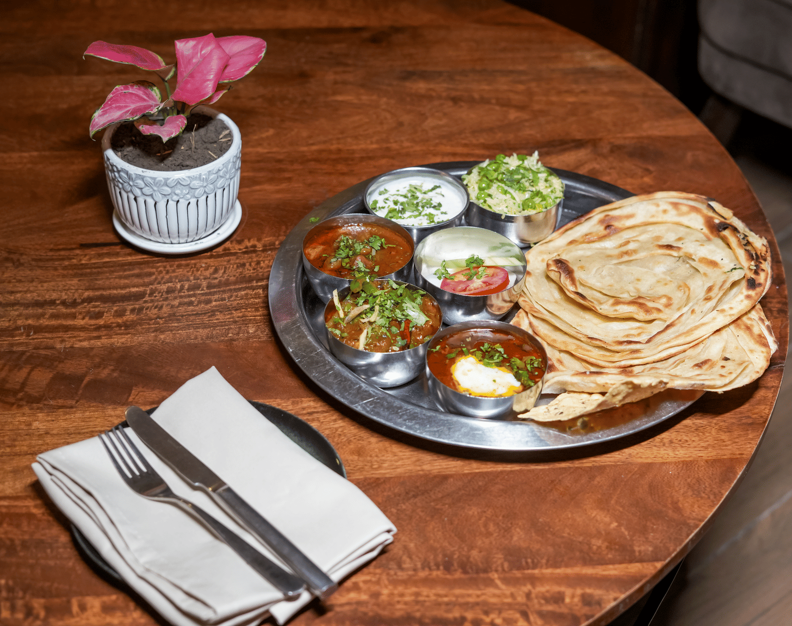 A metal thali platter with various curries and side dishes, served next to a stack of flatbreads or parathas at BluSalzz Select City Centre, Amritsar.