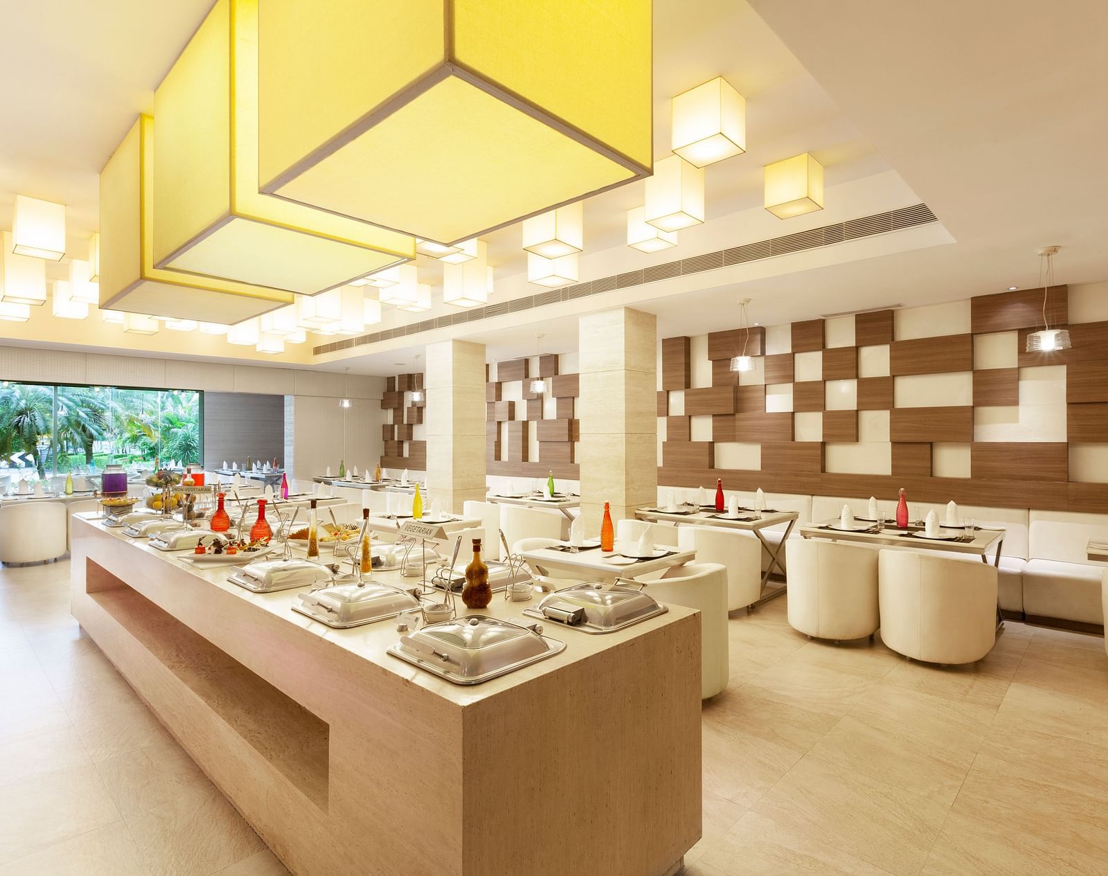A diagonal view of a restaurant with an island in the middle featuring buffet items, surrounded by tables and chairs on the sides | Cenneys Gateway