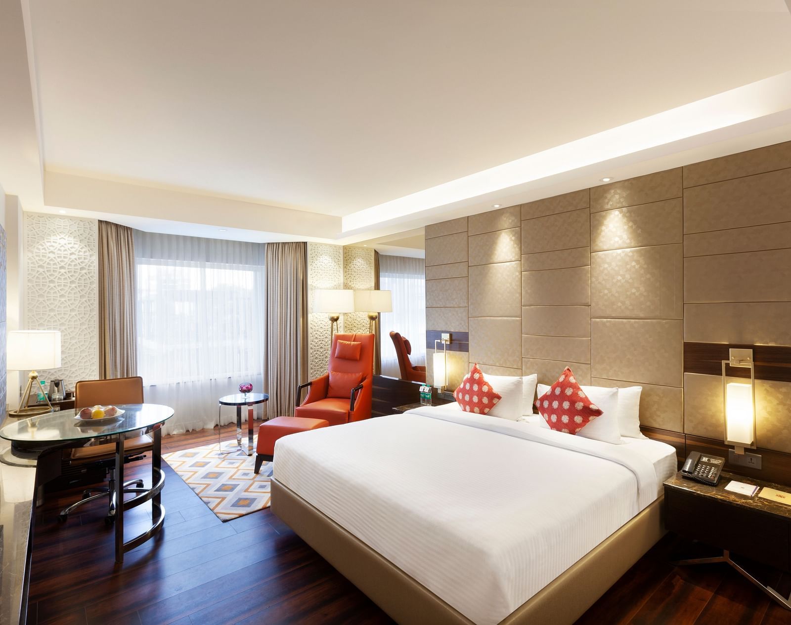 A spacious room with a large bed, wall-mounted TV, table, and cushioned chair, with curtains pulled to the side of the windows | Cenneys Gateway