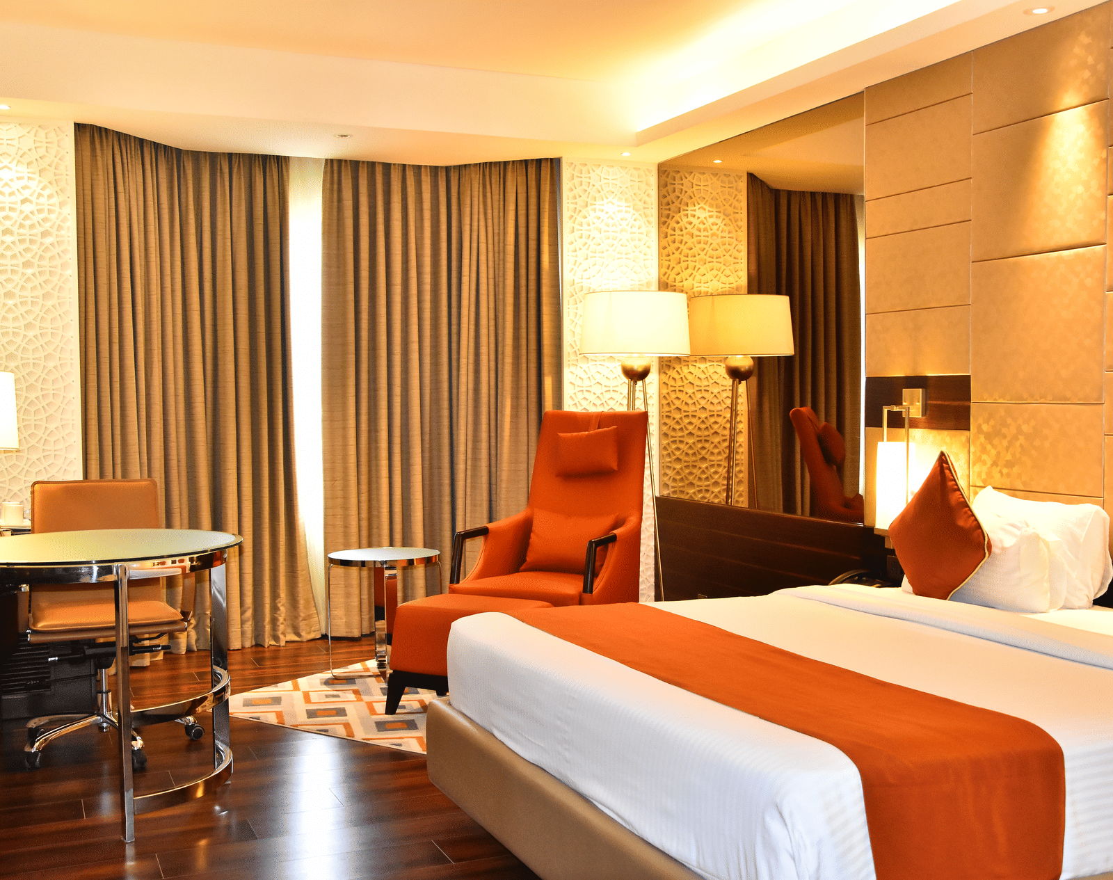 A spacious room with a large bed, a cushioned chair with a table beside it, and windows covered with curtains | Cenneys Gateway