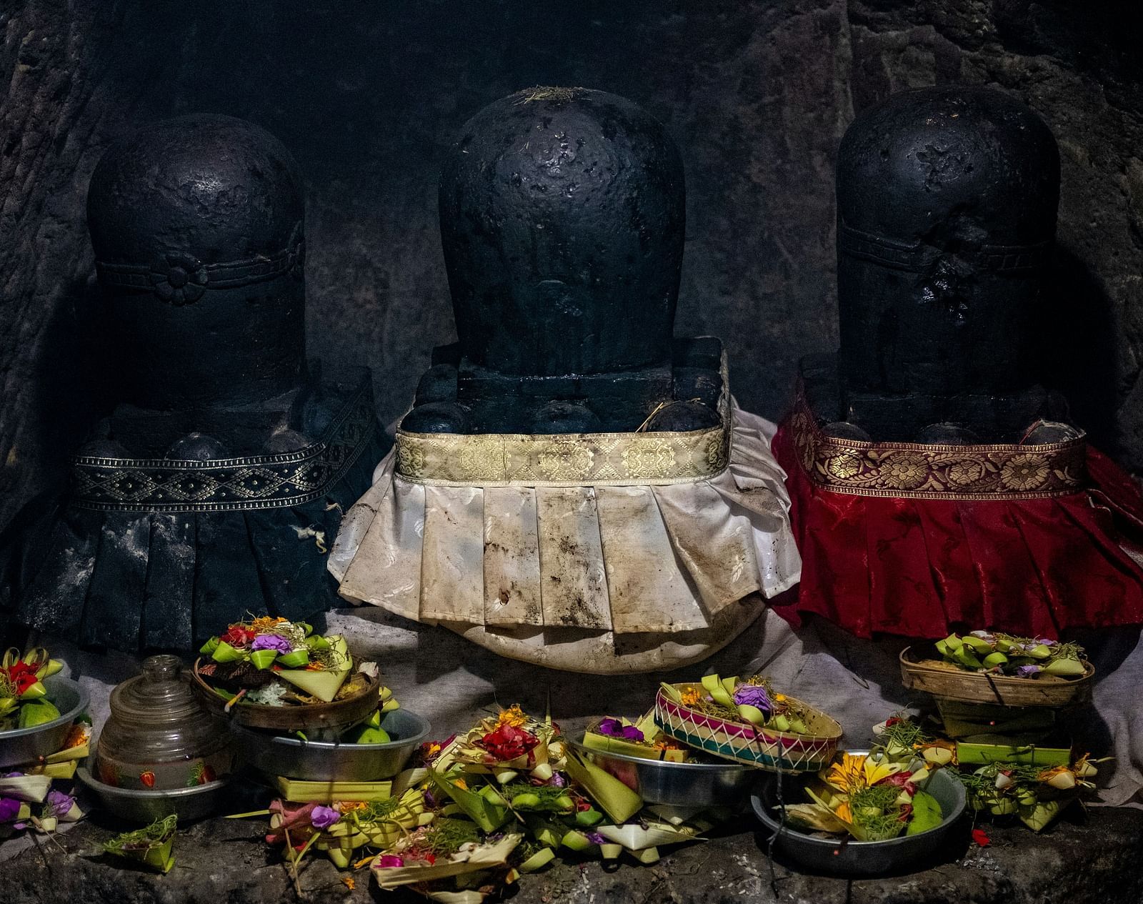 A close up shot of 3 shiva lingams with many fruits items kept in front of it inside a temple.