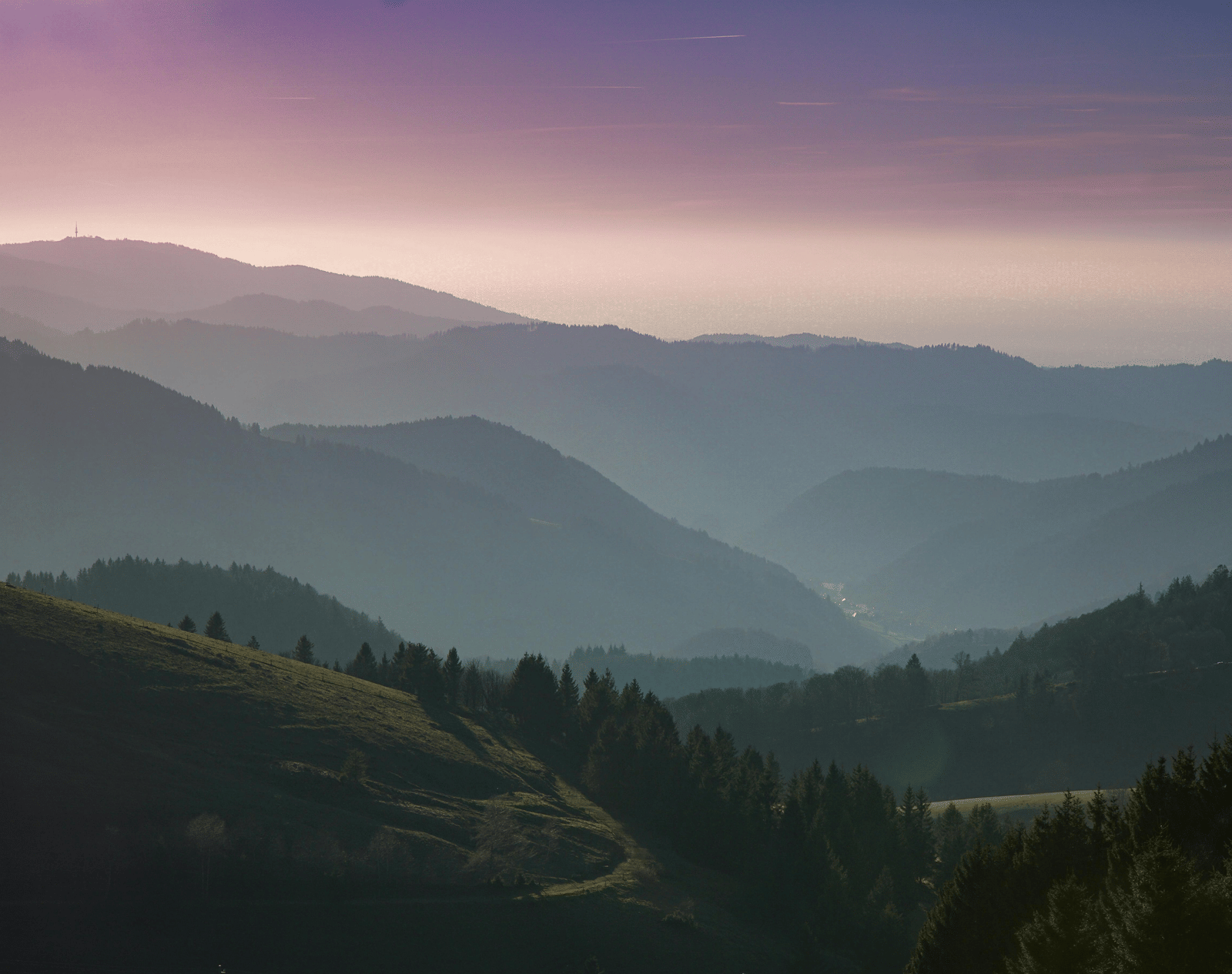 Layered mountain ranges fading into a sunset.