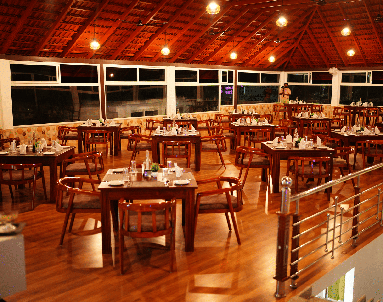 A large dining room with a wooden vaulted ceiling, wooden tables/chairs, and expansive windows at Coorg Orange Blossom Resort and Spa.