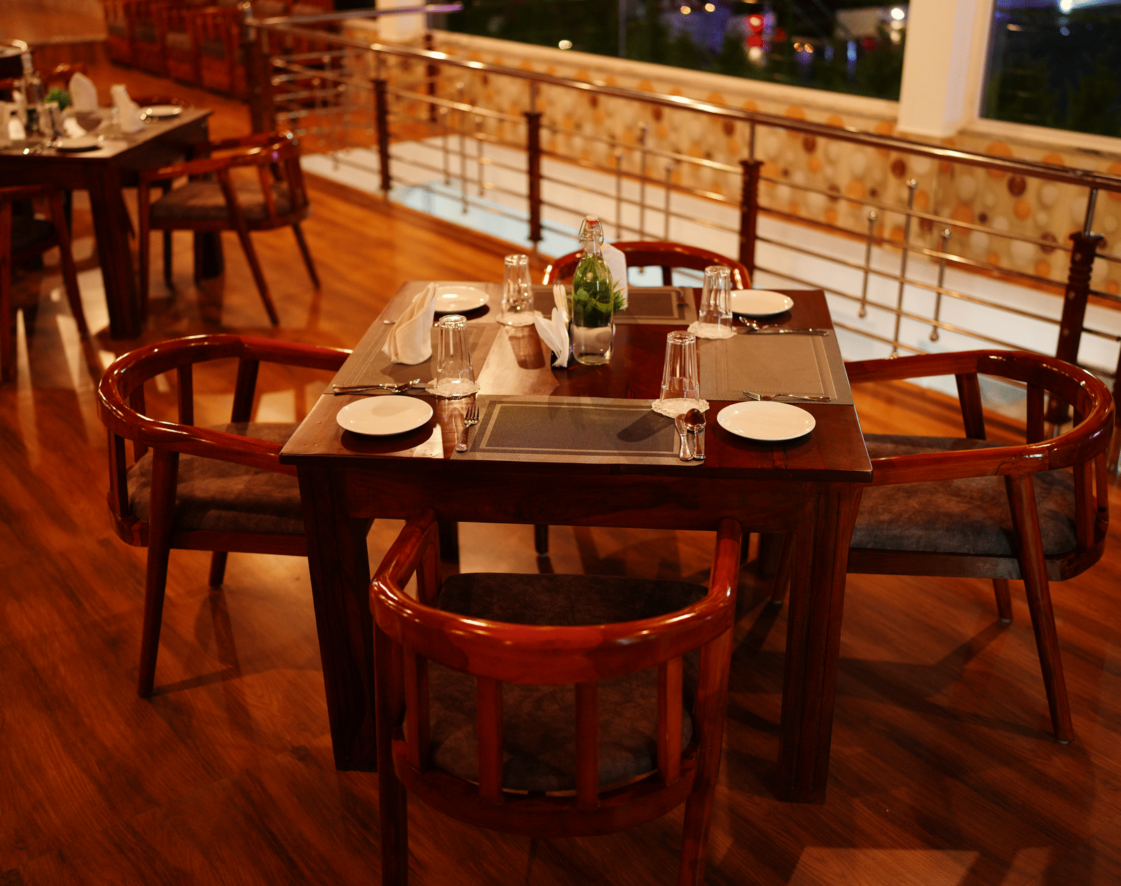 A close-up of a dark wooden dining table set with plates and cutlery in a dimly lit restaurant at Coorg Orange Blossom Resort and Spa.
