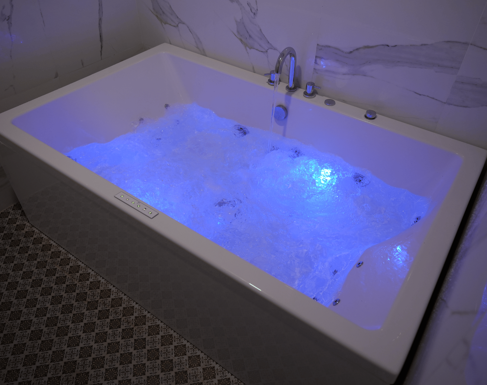 A large white bathtub or jacuzzi filled with bubbling water and illuminated by blue underwater lights at Coorg Orange Blossom Resort and Spa.