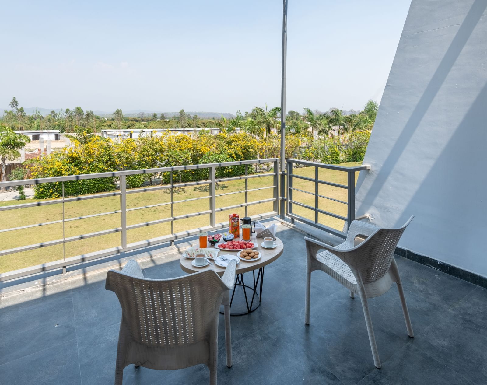 Balcony with chairs and table, offering a view of fields and trees - DLS Forest Vines Resort & Spa, Ramnagar (Jim Corbett)