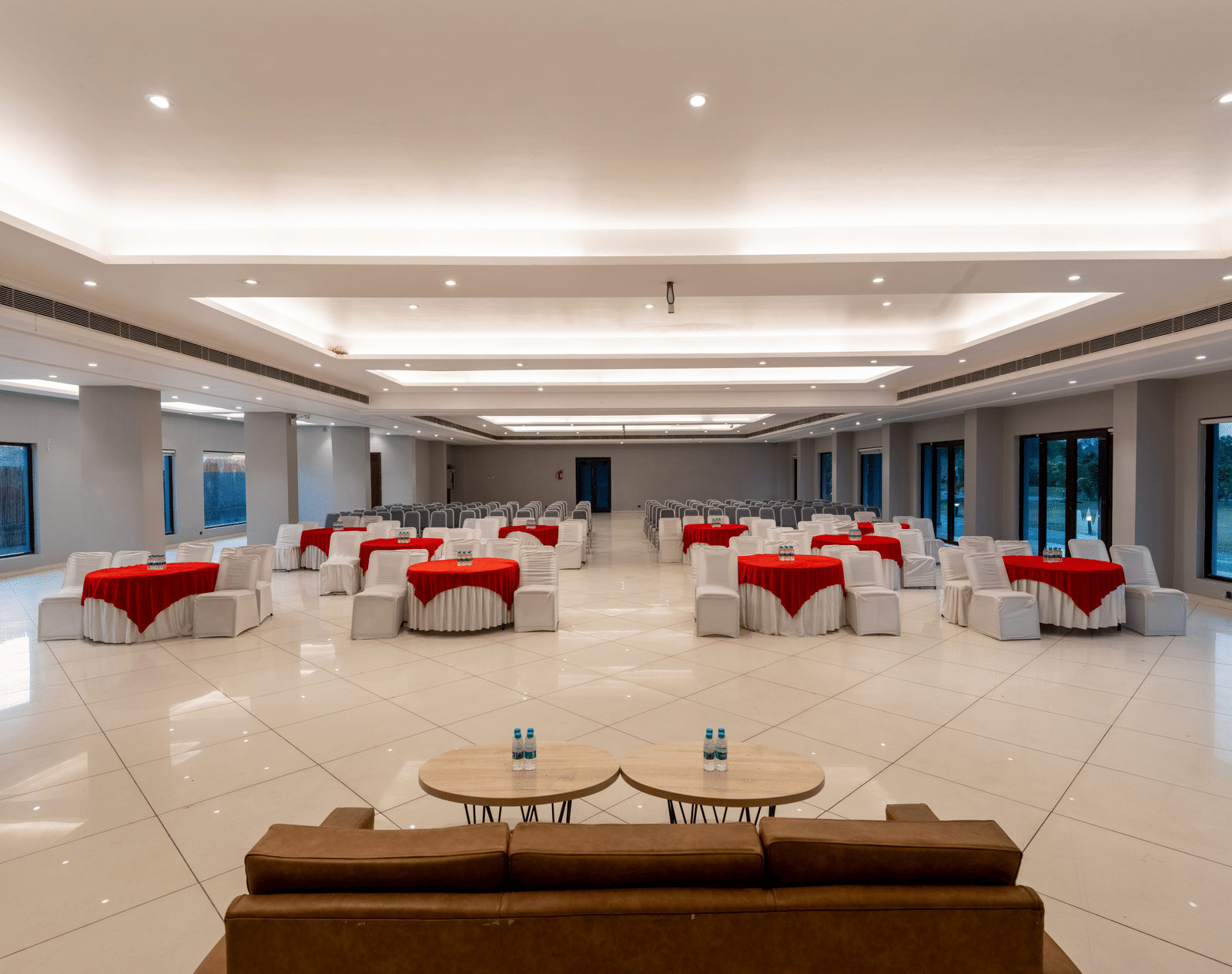 Tables with neatly decorated tablecloths, a plush sofa, and two round tables set in front at DLS Forest Vines Resort | Banquet Halls in Jim Corbett