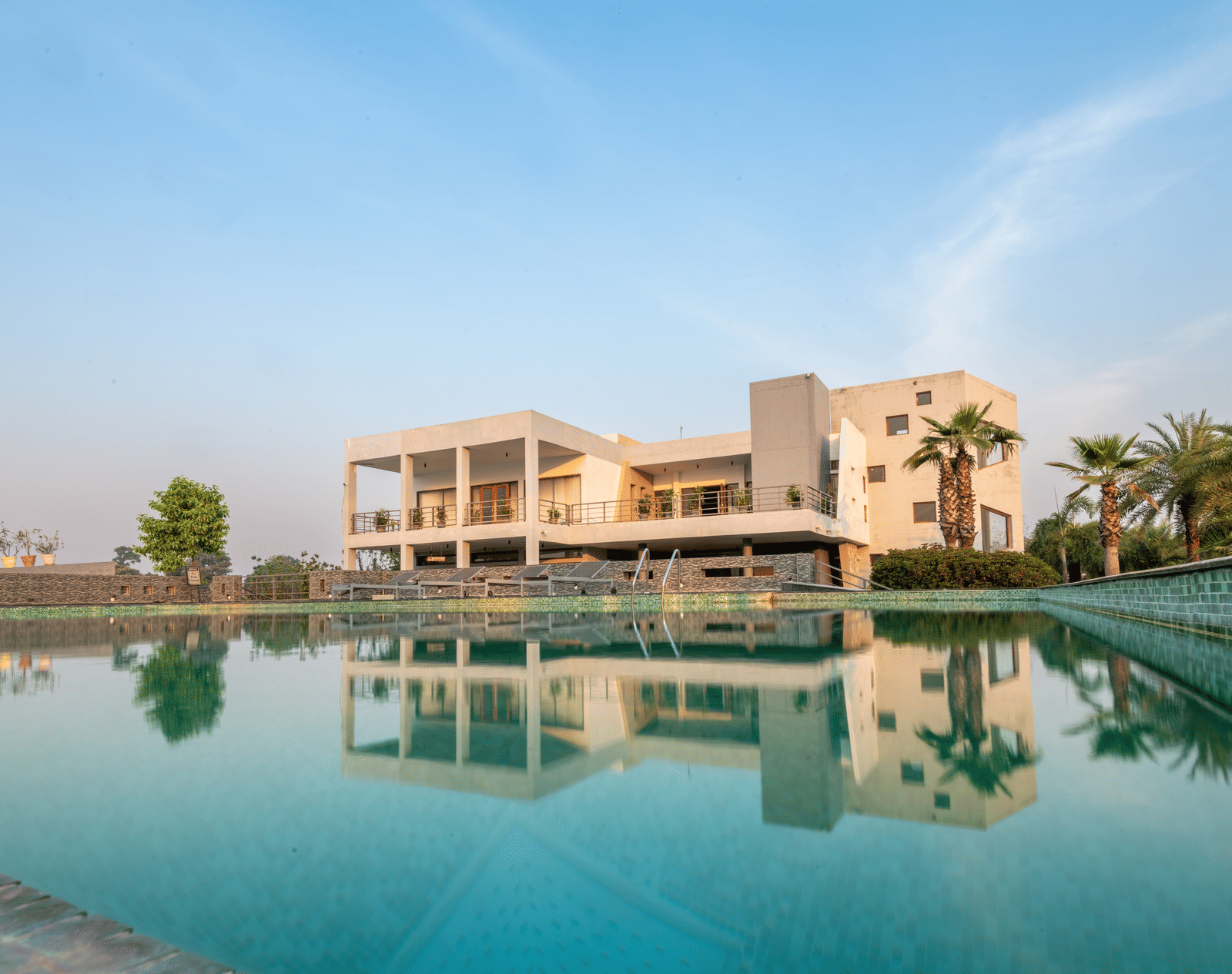 Facade view of DLS Forest Vines Luxury Resort in Jim Corbett, with its reflection shimmering on the swimming pool under a clear sky.