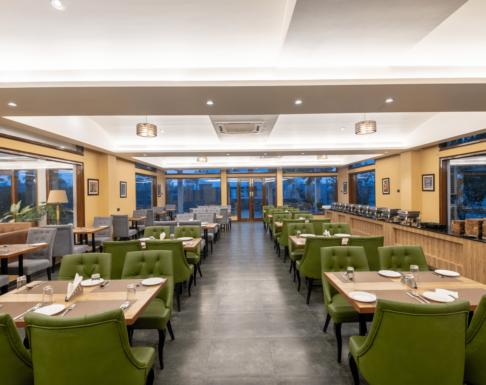 View from one end of the restaurant in Jim Corbett at DLS Forest Vines Resort, with tables and chairs neatly set on both sides.