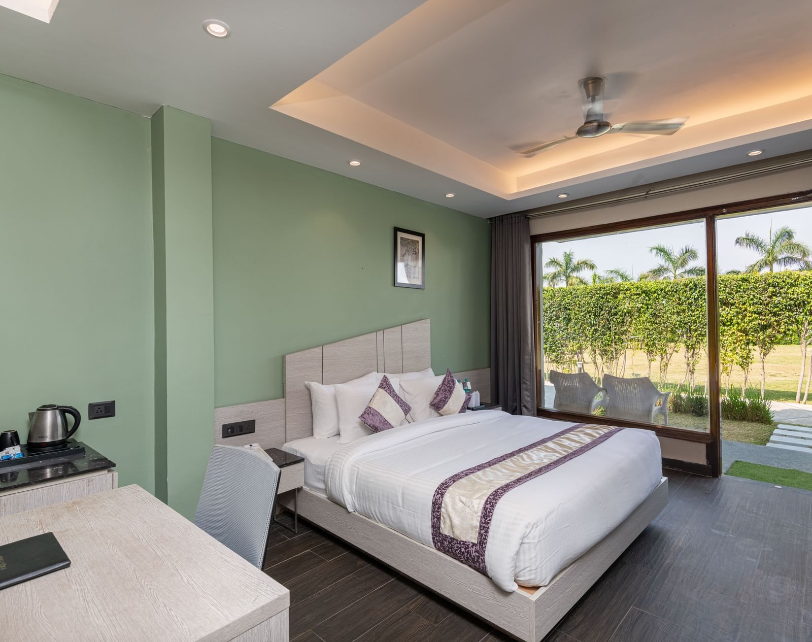 A spacious room at DLS Forest Vines Resort, complete with a large bed, bedside table, table and chairs, and a glass door opening to the balcony | Luxury Stay in Jim Corbett