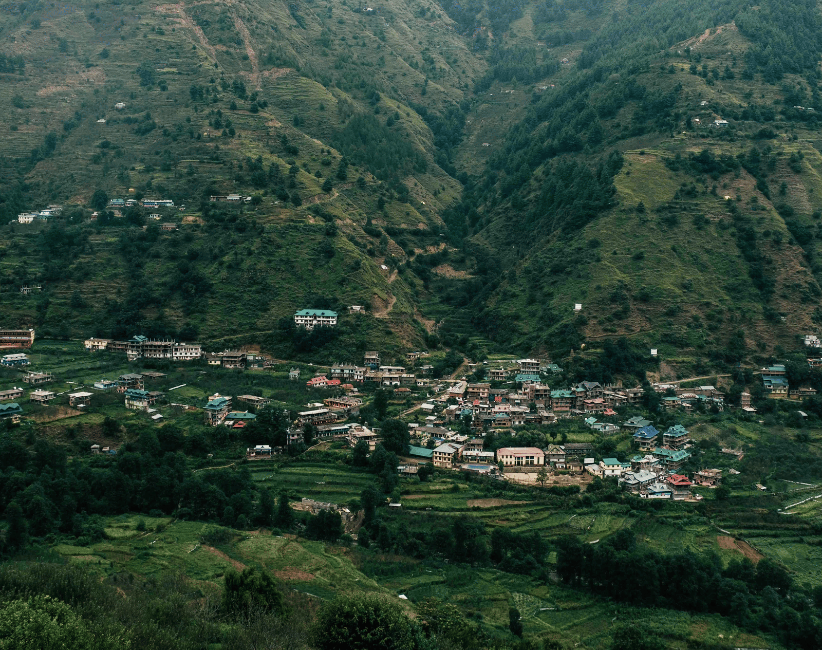 A lush green valley with terraced fields and scattered houses across the slopes.