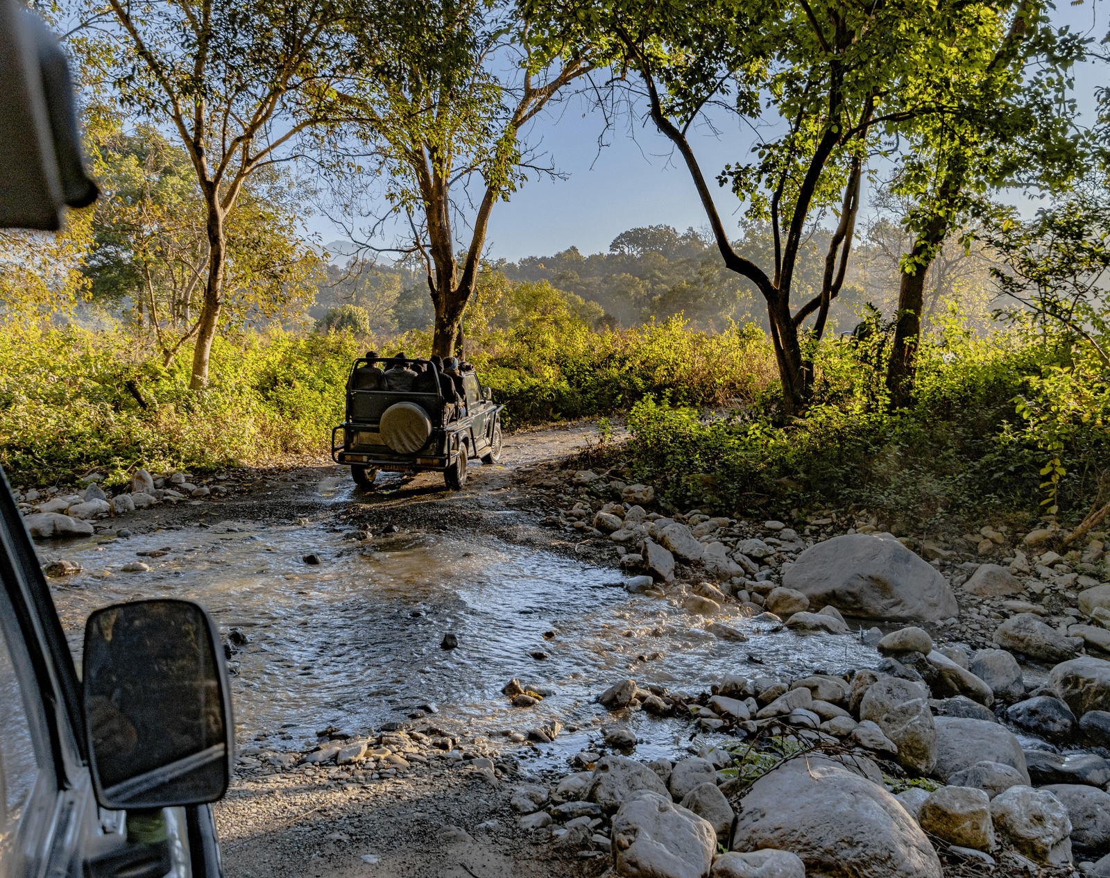 Image of two safari jeeps traversing through a stony water stream at Jim Corbett