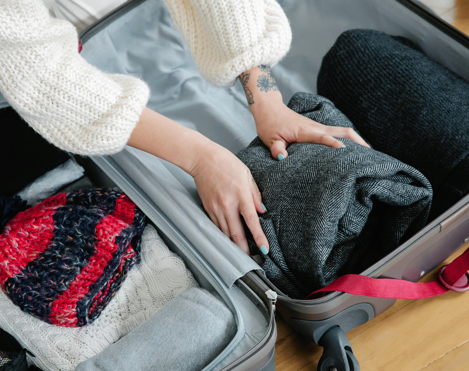 Person packing warm winter clothing like sweaters and woollen accessories into an open suitcase