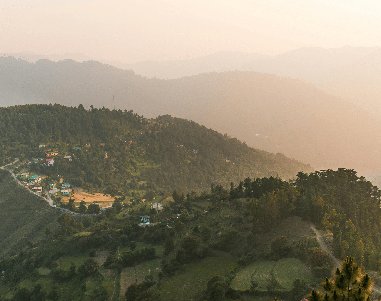  A panoramic view of rolling green hills and mountains at sunrise, with a faint haze in the distance.