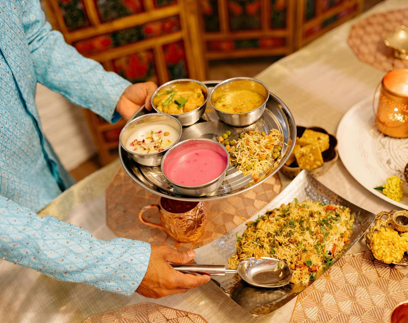 A person serving a traditional Indian vegetarian thali with various dishes at a well-set dining table in a restaurant setting.