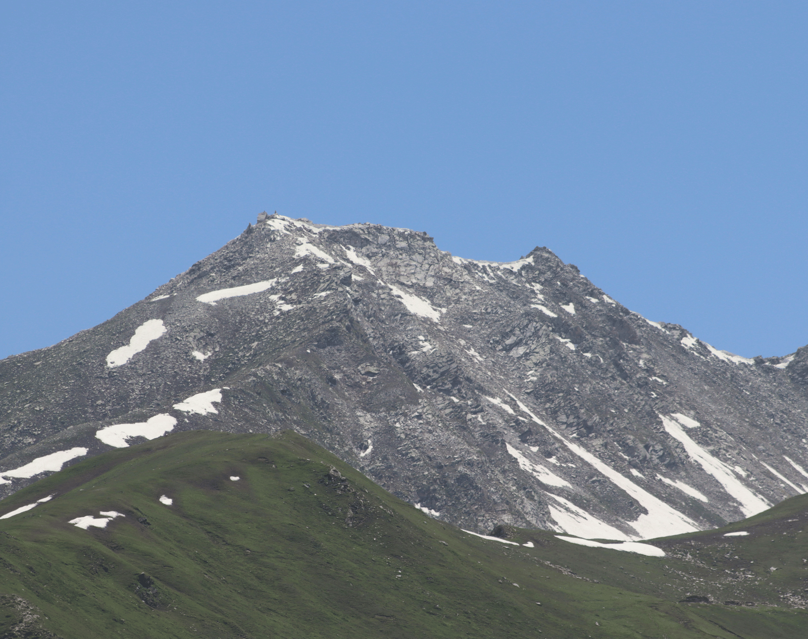A majestic, snow-capped mountain peak dominates the view under a clear, bright blue sky.