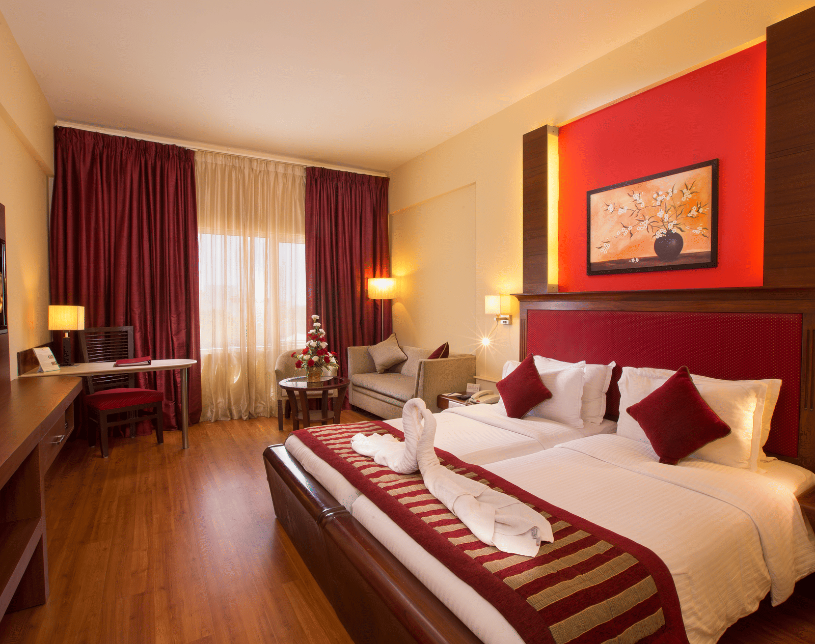 Executive Room at Hotel Atithi featuring a king bed with red accents, warm lighting, a work desk, seating area, and contemporary decor.