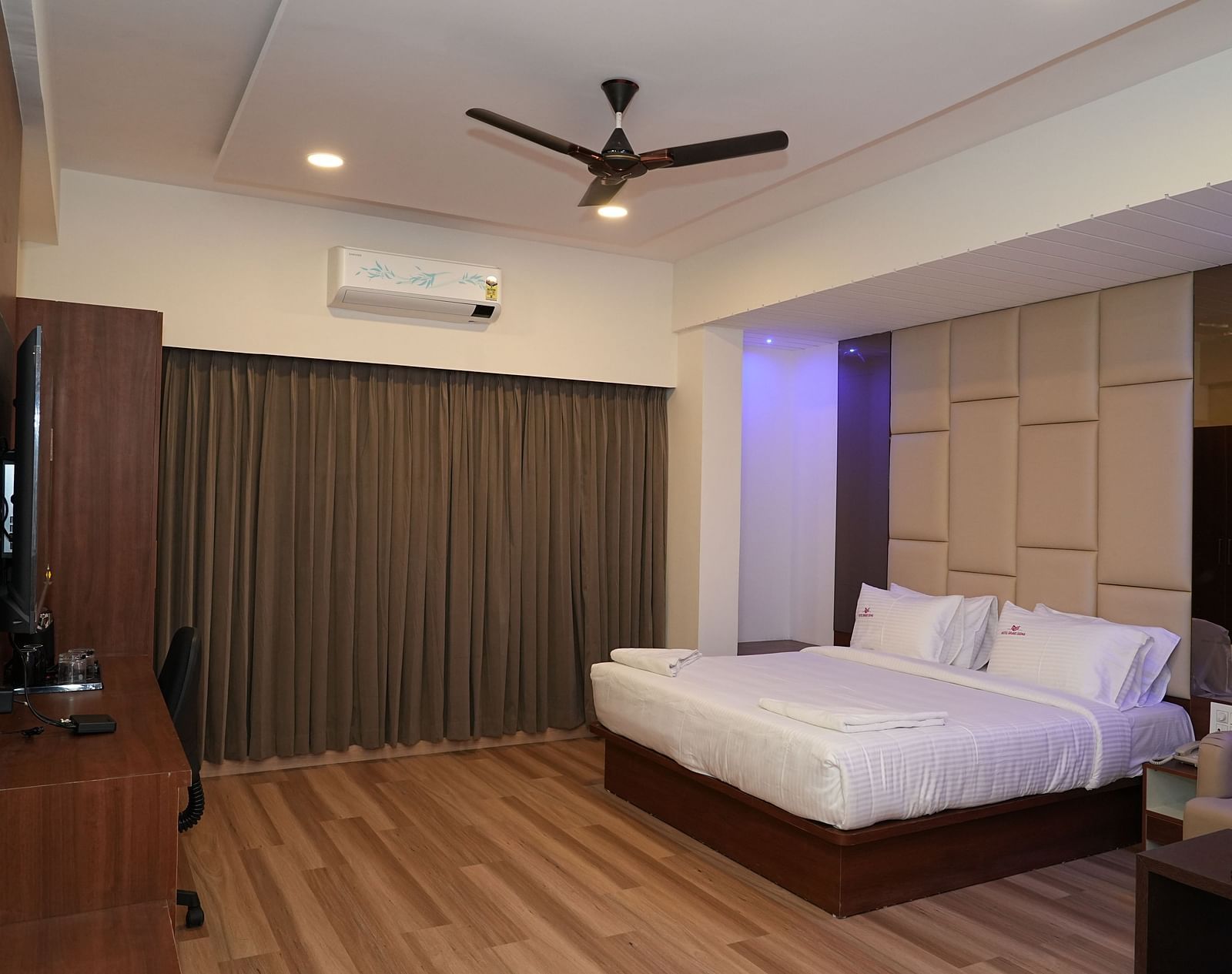 full view image of the suite with a comfortable double bed and a wall mounted television right opposite to it with closed curtains - Hotel Grand Sigma