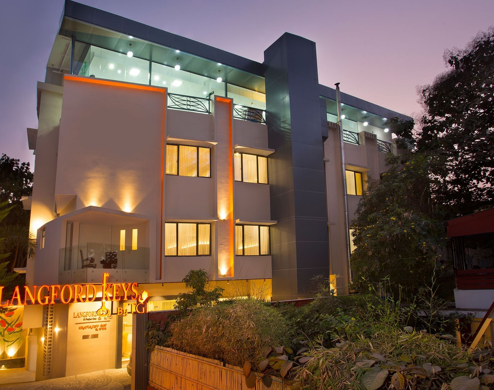 The exterior entrance of Langford Keys Hotel showing the signboard with reflective windows and modern architecture at dusk - Hotel Langford Keys by TGI, Shanti Nagar