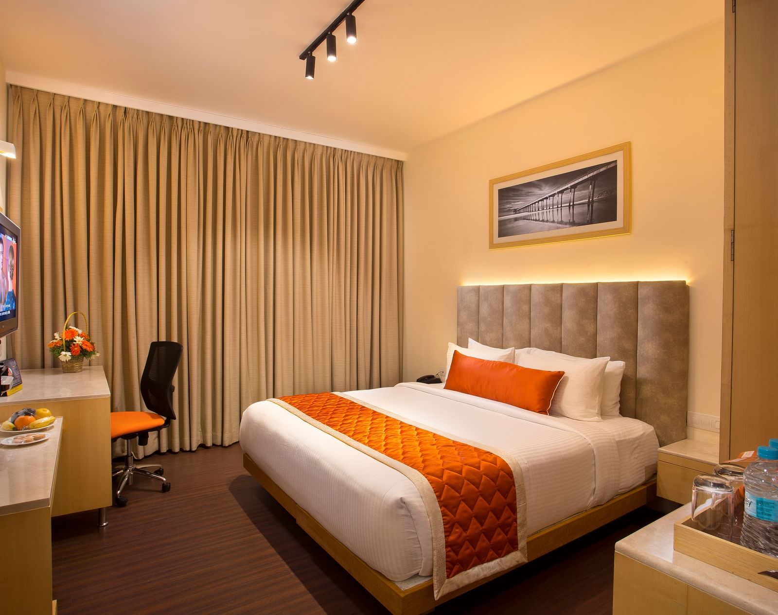A cosy hotel room with a plush bed adorned with an orange bed runner, a work desk and a wall-mounted TV - Hotel Langford Keys by TGI, Shanti Nagar