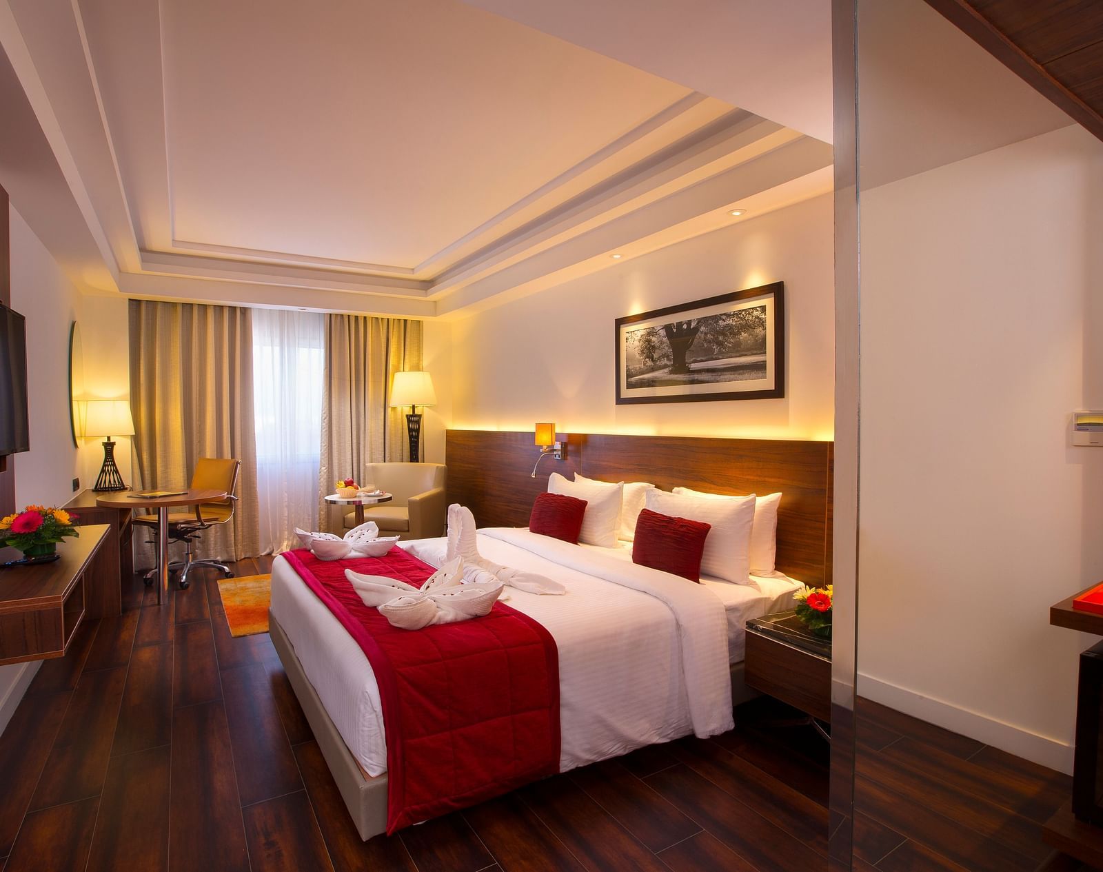 Another view of an elegant hotel room with a large bed, red throw blanket, decorative pillows and a framed black-and-white photograph on the wall - Hotel Southend by TGI - Bommasandra, Bangalore