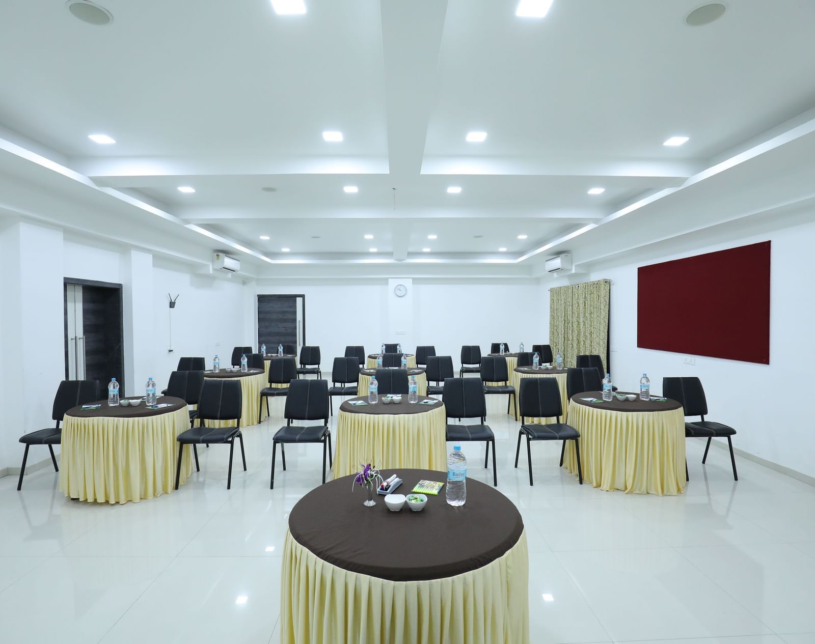 A meeting room at Imperial Grande with several round tables and chairs, arranged in a cluster style, and a red notice board on one side of the wall.