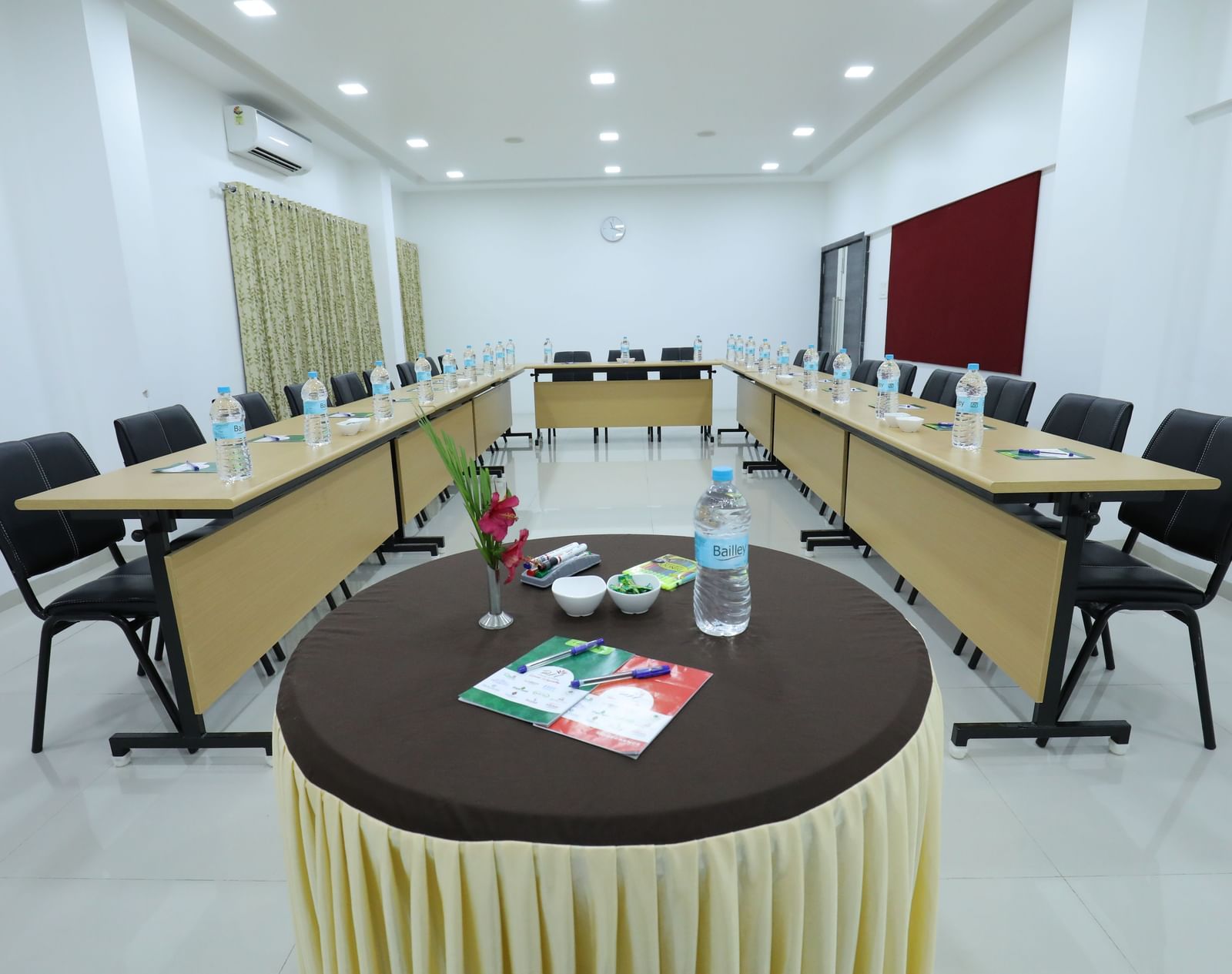 A conference room at Imperial Grande set up with a round table with additional amenities like bottled water and stationary, featuring chairs arranged in a U-shaped style.