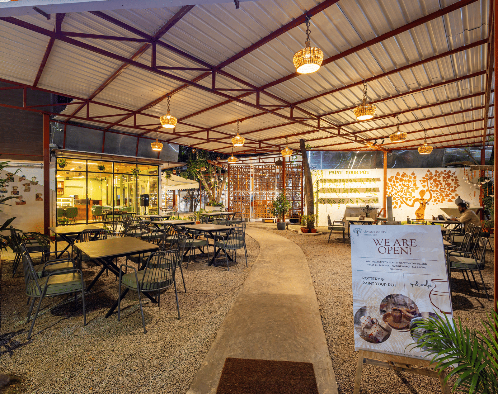Claysutra Cafe & Restaurant at Kove Smart Stays seen during a darker time of the day, with ambient lighting, outdoor seating, and an overhead shed.
